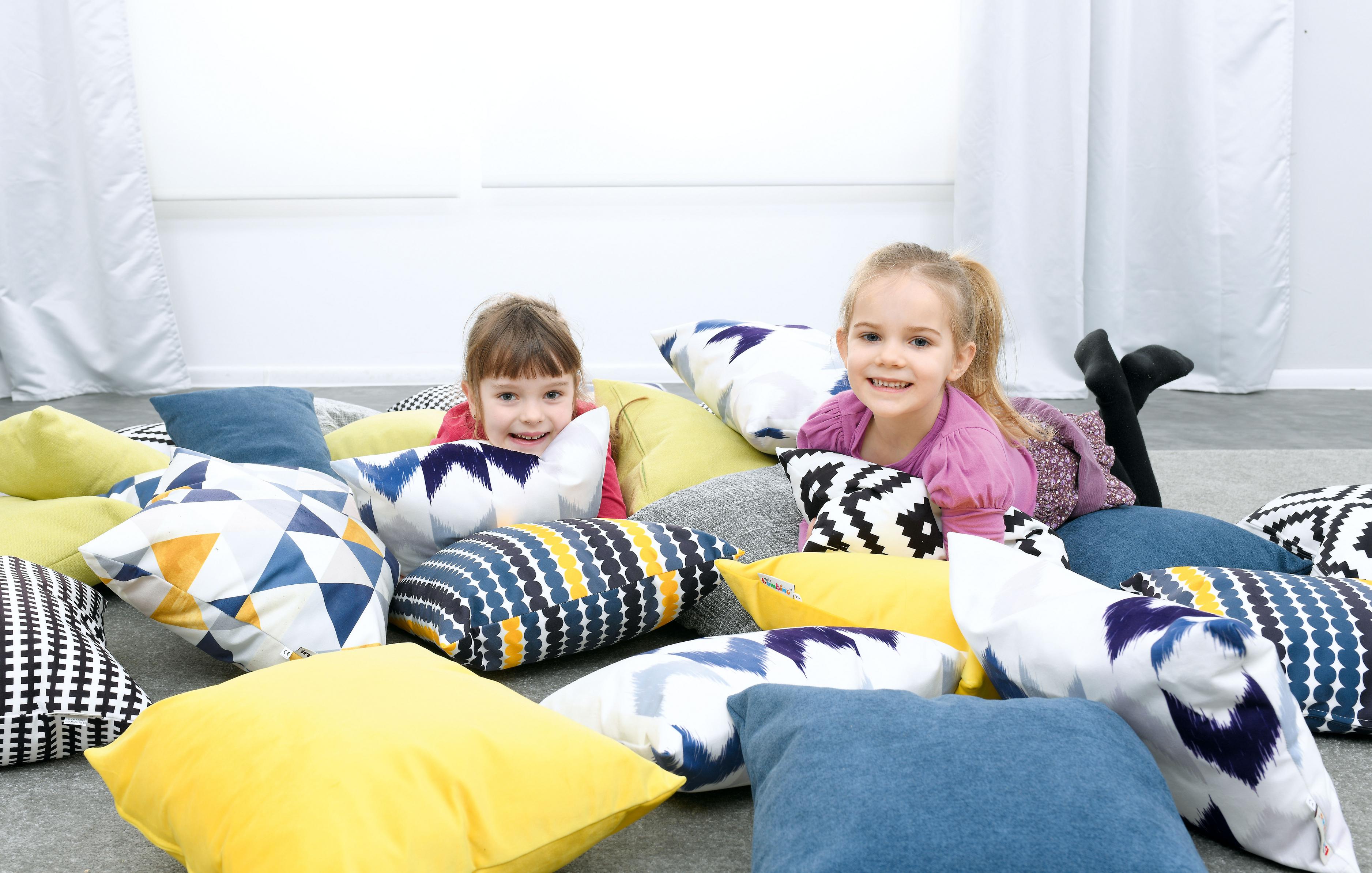 Kinder spielen auf bunten Kissen für Sitzlandschaft.