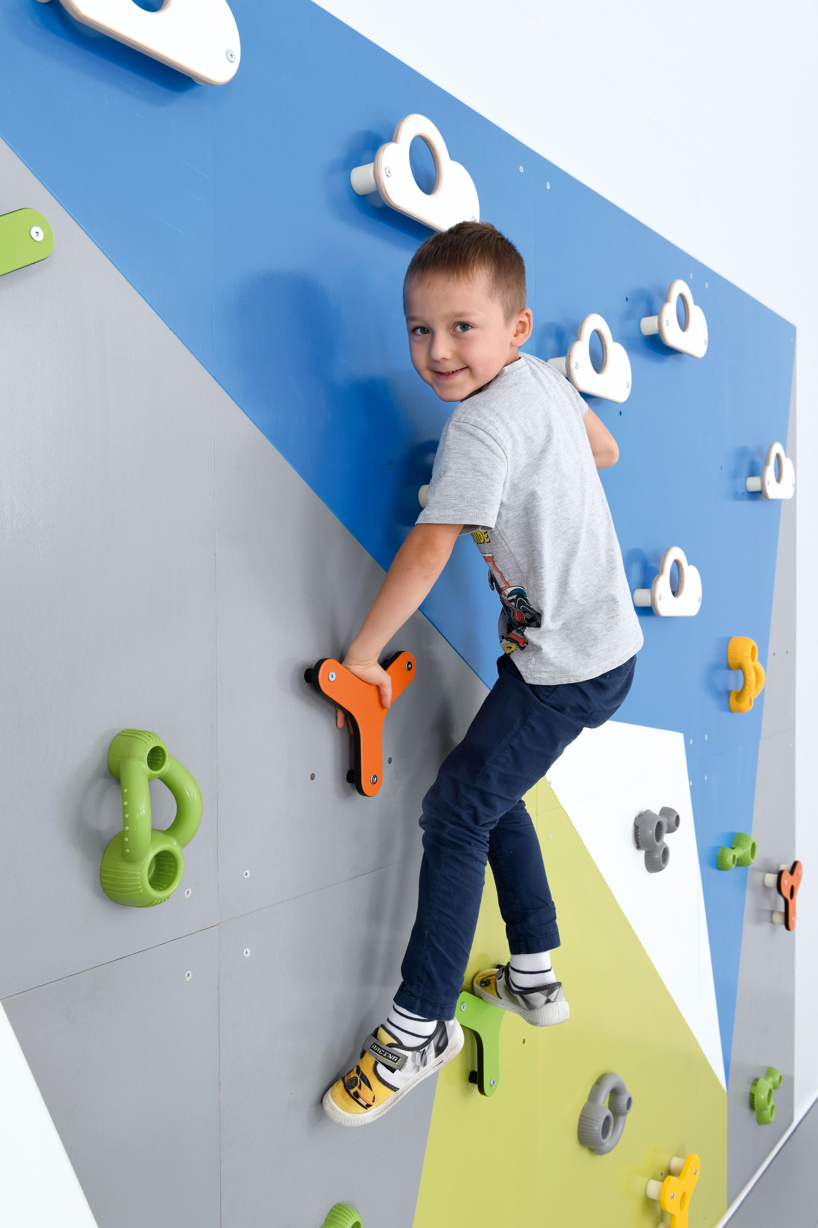 Kind klettert auf bunter Kletterwand in Sporthalle.