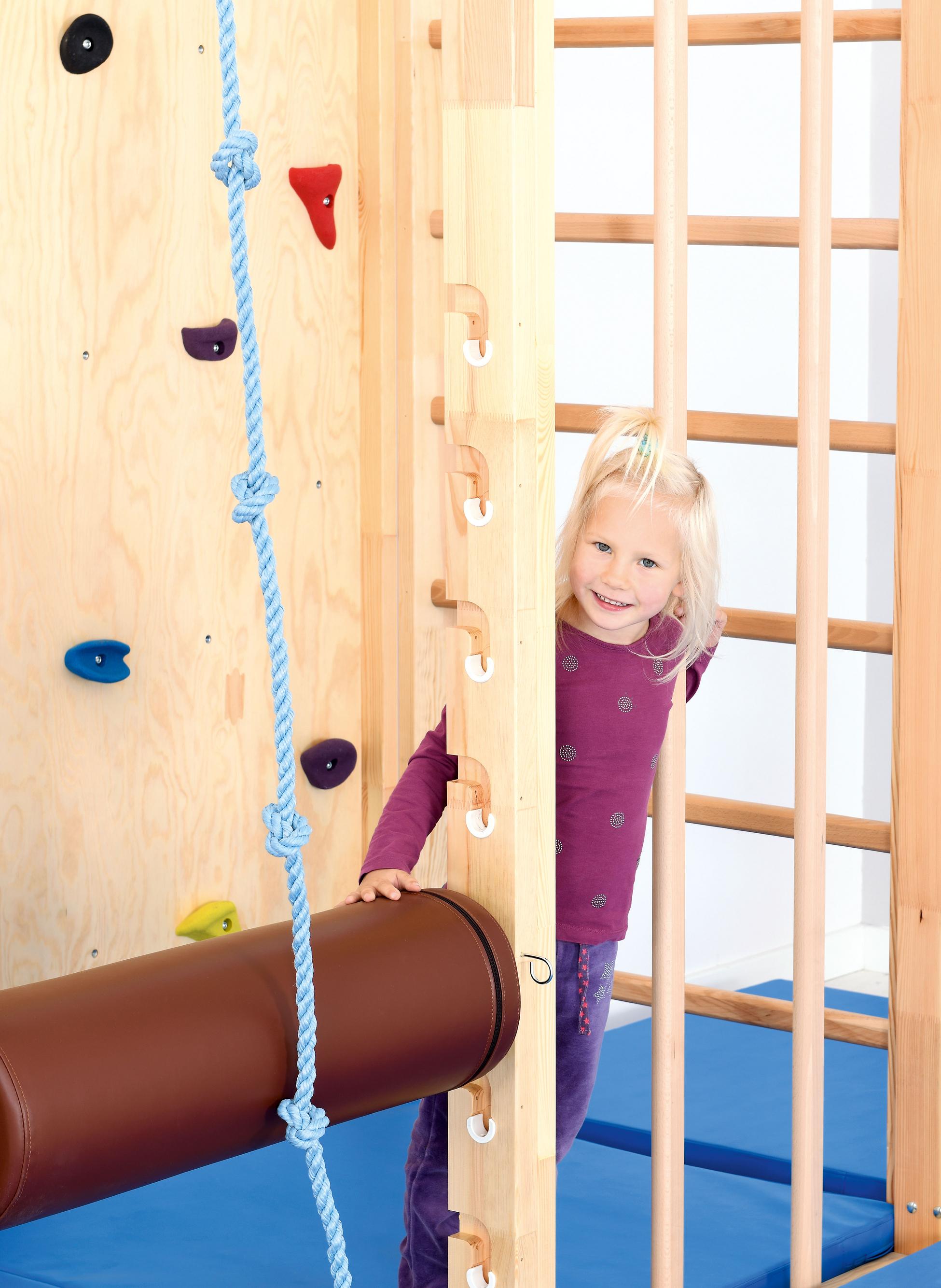 Kind klettert fröhlich auf Kletterwand in Turnhalle.