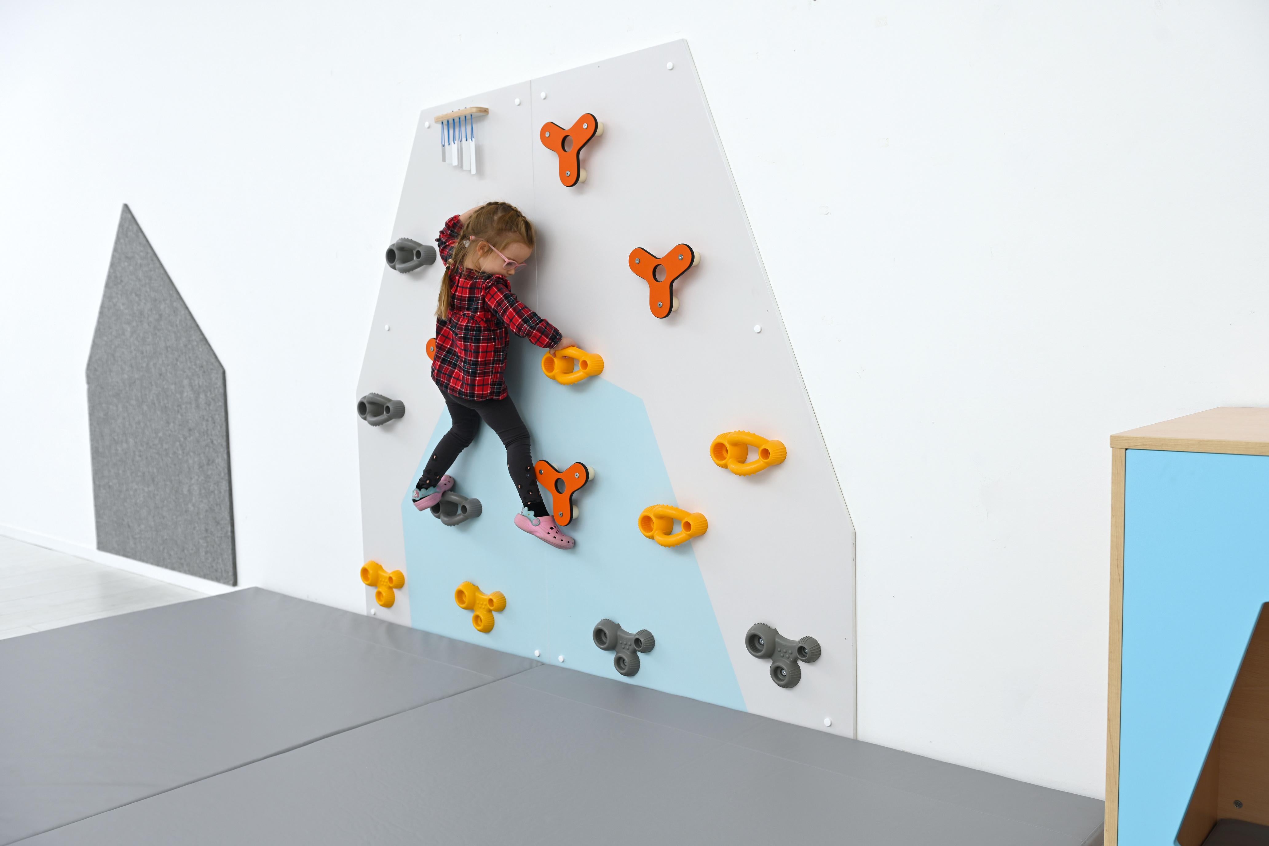 Kletterwand für Kita mit spielendem Kind, bunte Griffe.