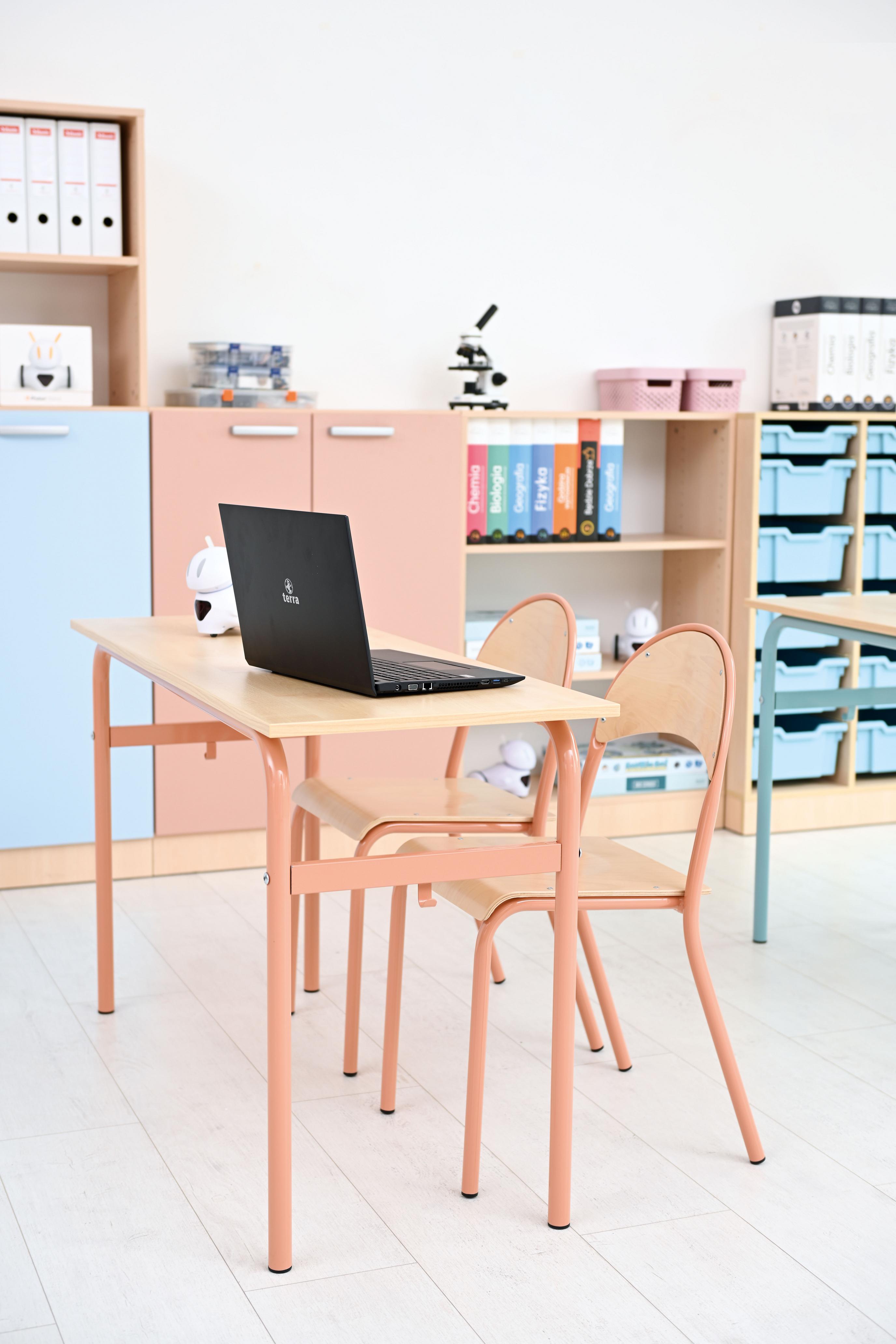 Doppeltisch mit Stühlen und Laptop im Klassenzimmer.