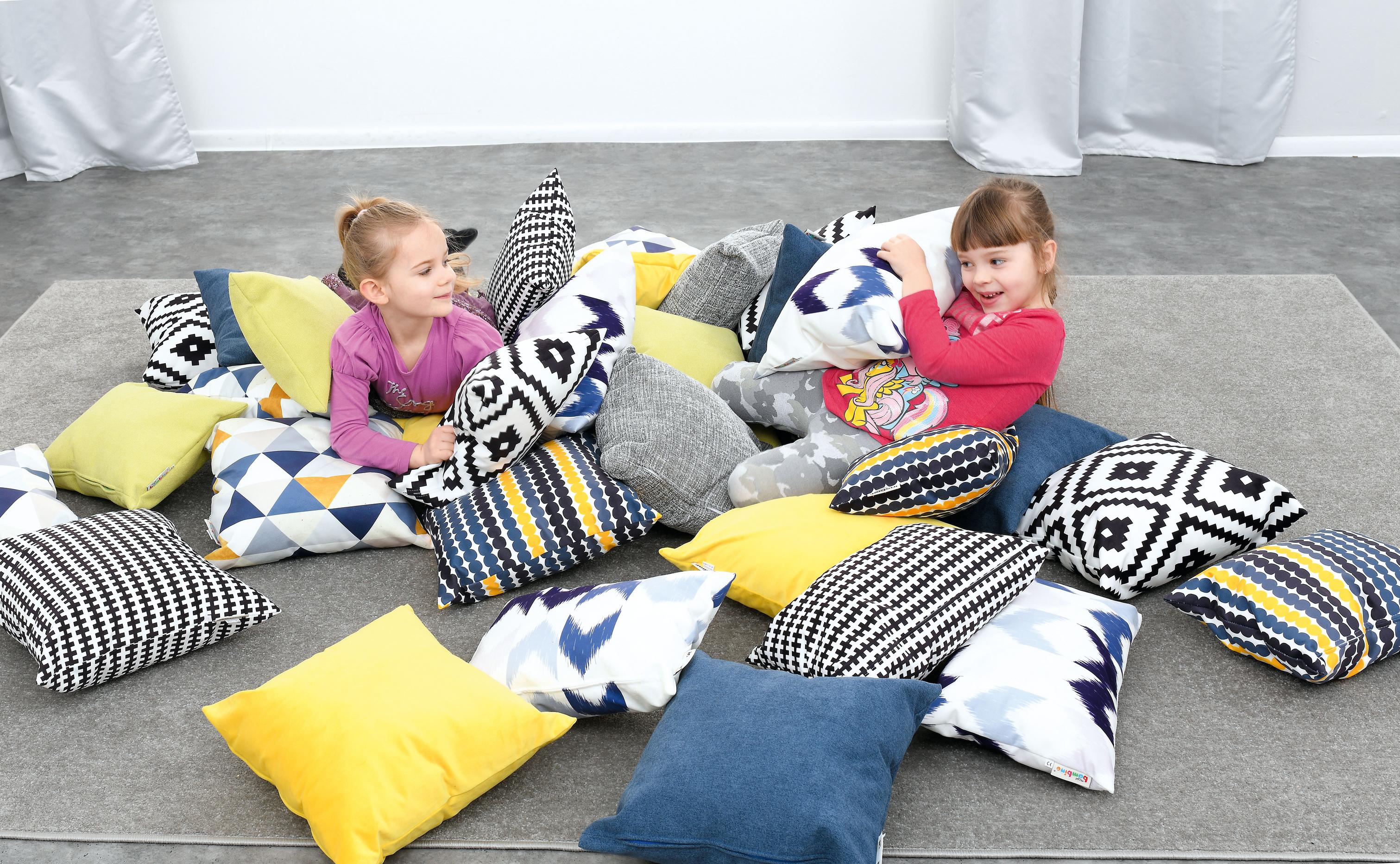 Kinder spielen auf bunten Kissen für Sitzlandschaft.